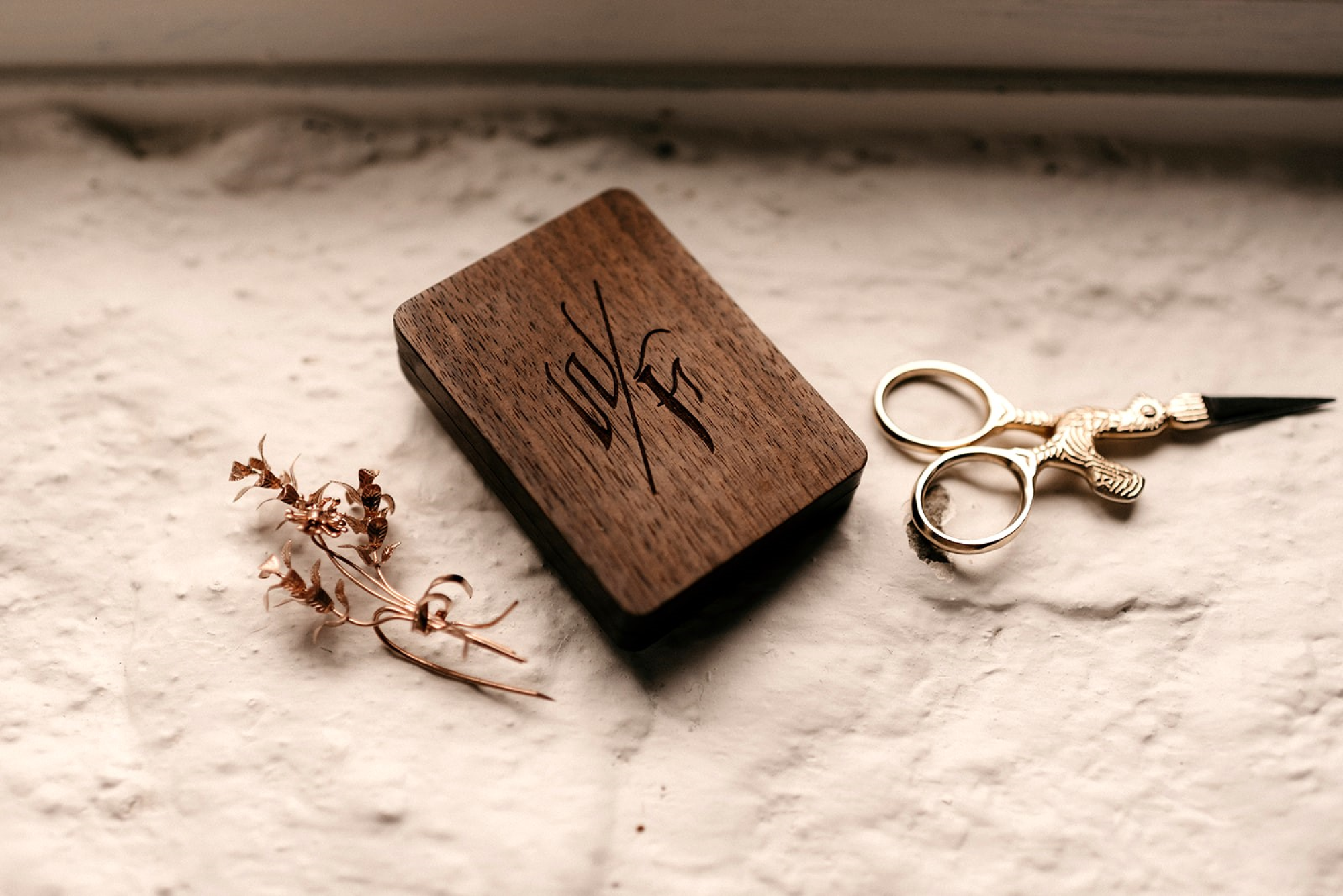 Wooden brown box with wedding initials in black writing, brass flower pin and silver mini scissors on either side