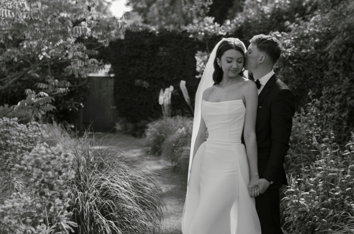 Newlywed couple in wedding attire posing amongst flowers in garden