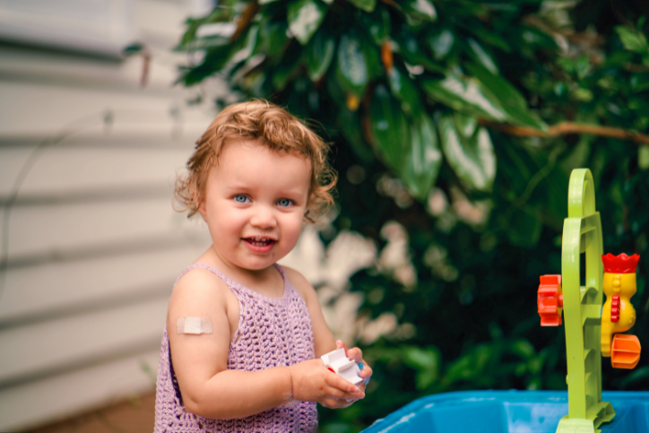 Little girl with bandage on arm smiles at camera