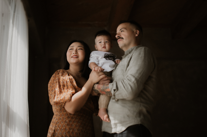 Family of three look out of a window together in a dark room