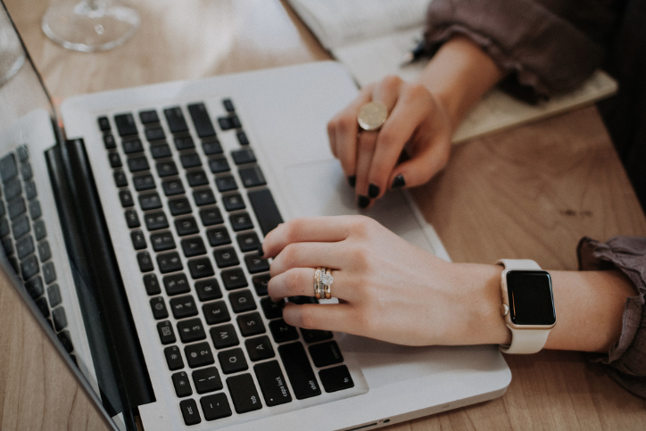 Woman with engagement ring types on laptop