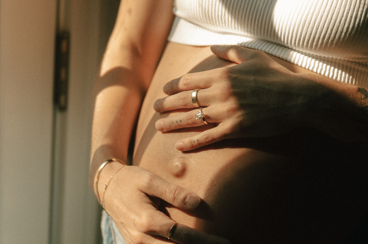 Close up of pregnant belly with hand on top wearing engagement ring